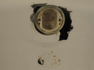 Picture of a damaged bathtub. The picture shows a closeup of the part where the water connections is. You can see rust and dirt has build up around it. 