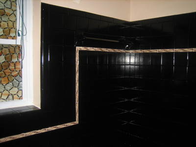 Picture of a bathroom and more specific of a shower that got refinished. The tiles are black, creating a lot of dramatic contrast in the bathroom. 