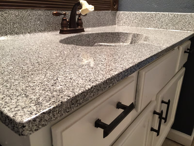 Picture of a bathroom countertop with one sink. The color of the finish is light grey and the cabinets are white, creating a modern look and feel. 