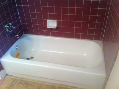 Picture of an outdated, nineties looking bathroom. The tiles have an eggplant red color and the tub looks dirty with some caulk build up inside. 