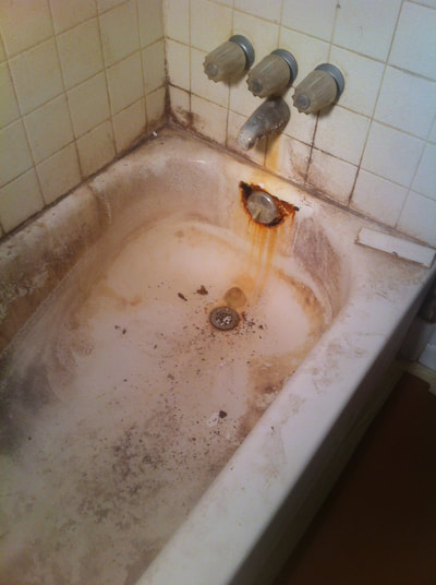 In this image you can see a bathtub before reglazing. you can see black stains along the edge and bottom of the tub. You can also see rust stains in near the front of the tub. 