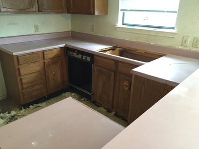 Picture of a Kitchen before restoration. in this image you can see a pink countertop, dull green walls. and floor. 
