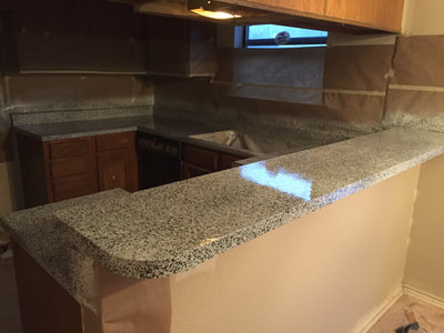 Image of a fully resurfaced kitchen. You can see black and white countertop with new lighting and sink.