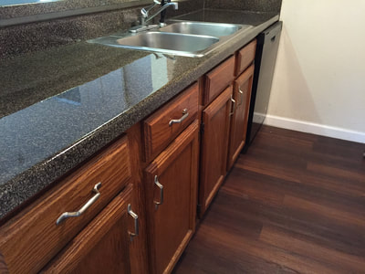 This picture shows a kitchen countertop that has been resurfaced using the Sable Stone pattern. You can see The gray black stone pattern with brown flooring and cabinets.