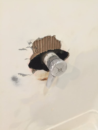 Picture of a fiberglass bathroom wall with a hole where the connection for the water is. It looks not attractive and needs repair. 