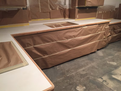 Picture of a kitchen in the process of refinishing. The cabinets are covered, so that they are protected and the countertops are exposed to start the refinishing process. 