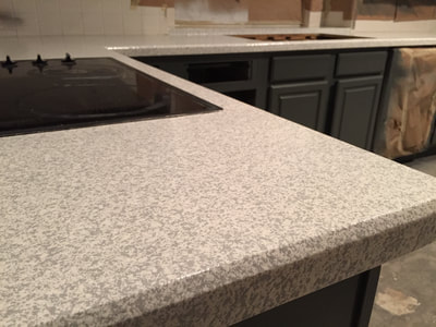 An after picture of refinished countertops. The white finish stands in contrast with the darker cabinets, which create a modern look and feel to the kitchen. 