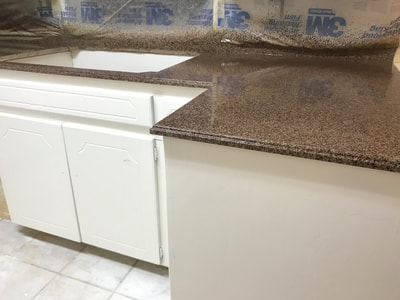 Picture of a kitchen countertop resurfacing project. You can see the countertop getting refinished with the Bronze Gravel pattern on a white kitchen background. 