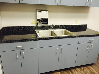 Picture of a break room countertop that got refinished. The countertop is dark and the cabinets are white.