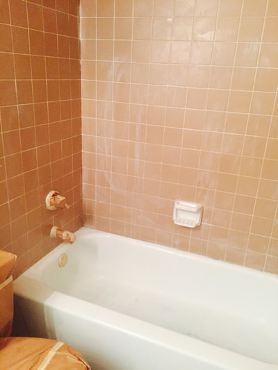 Picture of a bathroom tub and orange colored tiles. The tiles are dirty and caulk is present. 