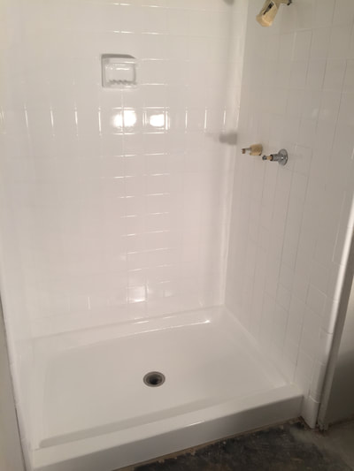 Picture of a tiled shower that got refinished. It looks shiny white and clean. 