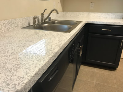 After picture of a kitchen where the countertops are refinished. The countertops have a light color, and the cabinets are darker, which is a popular look.