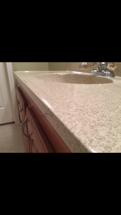 Picture of a bathroom countertop resurfacing job. You can see the bathroom countertop and sink resurfaced with the Lucid Pebble color pattern with  red brown cabinets 