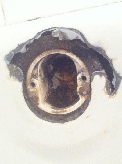 Picture of a damaged tub. You can spot a lot of rust and dirt clogged up in the hole. 