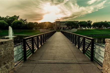 Picture of the of Irving Texas. its a beautiful view of sunset with the bridge on the river and grass on the bank of the river. Featuring blue sky