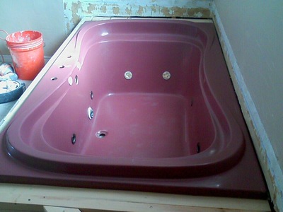 Picture of a pink jacuzzi that has some caulk build up and dirty sport along the edges. 